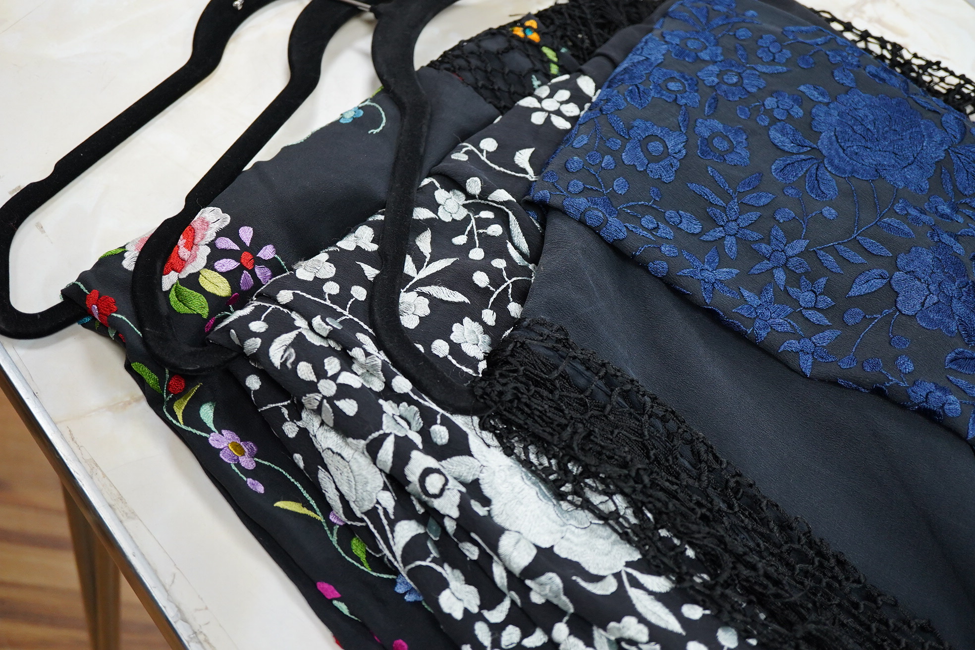 Three Chinese shawls, 1930’s machine floral embroidered, on black silk crepe de chine. One multicoloured, one navy blue, the other white embroidery. Largest navy and white shawls:130cm x 120cm. Condition - no stains, fad